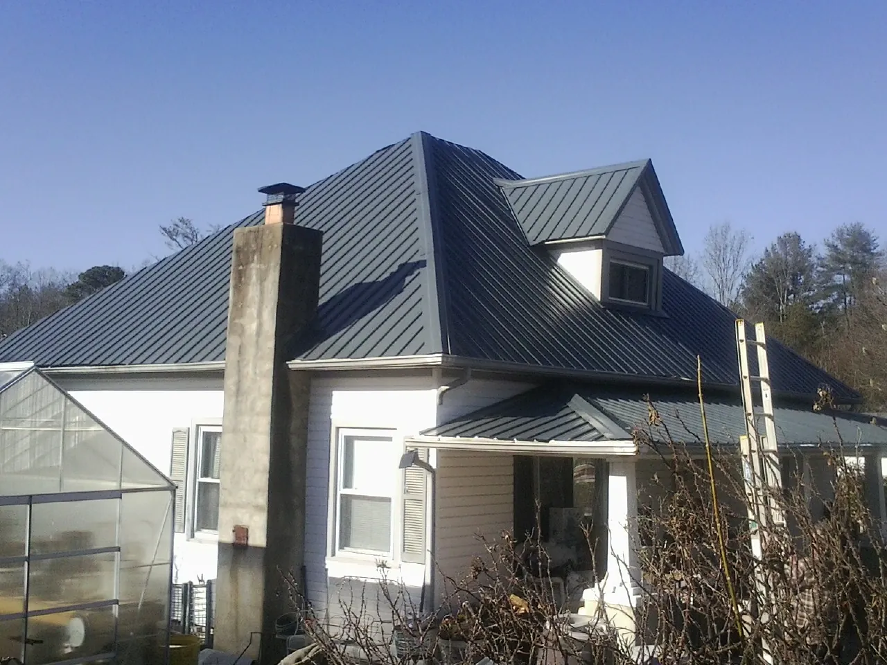Dark blue standing seam metal roof on a white farmhouse with dormer — Slate & Tile Roof Repair by Roofing Brothers in Lakeview