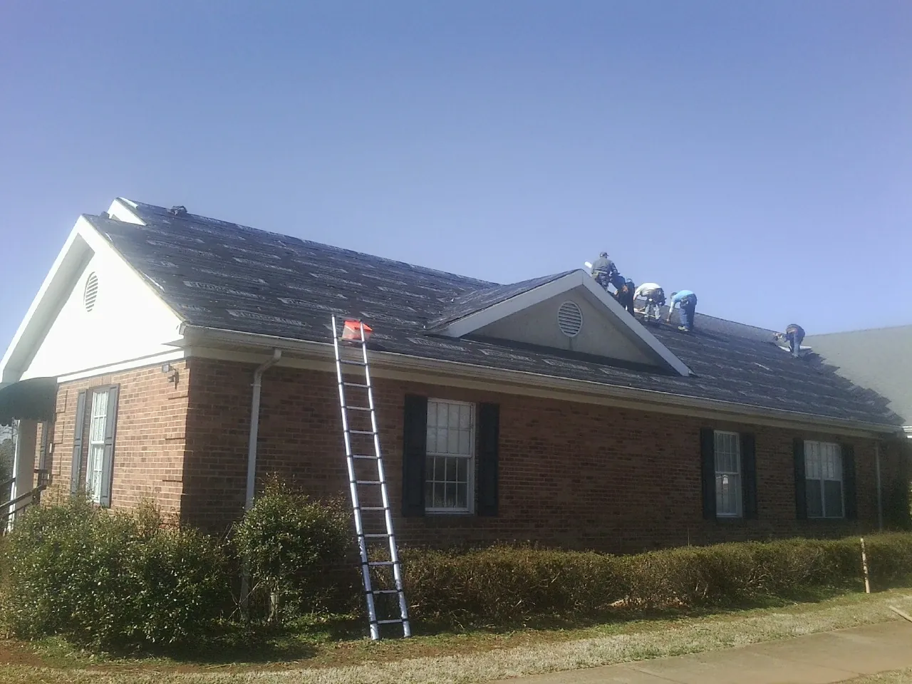 Crew tearing shingles off a brick ranch roof with a ladder set — Emergency Roof Repair work by our crew in Lakeview