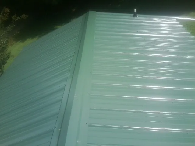New green metal panels meeting at the ridge of a roof — Flat Roof Repair work by our crew in Lakeview