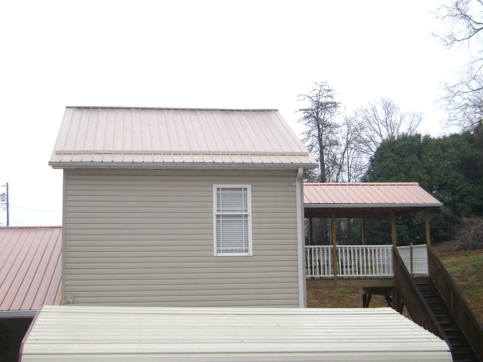 Tan metal roofs on a two story addition and attached porch, from a Roof Replacement job in Lakeview